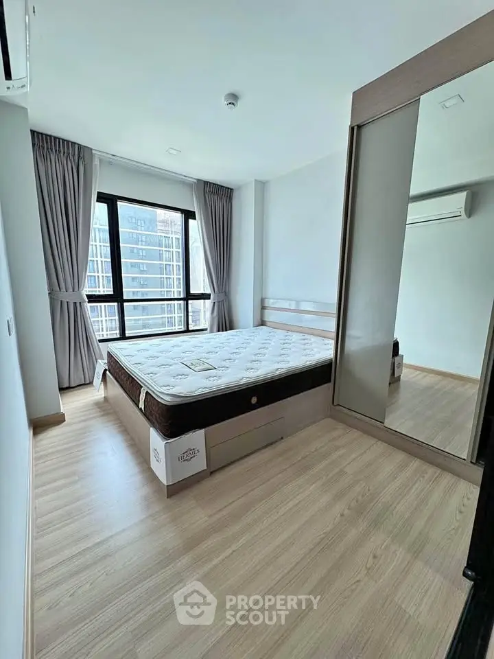 Modern bedroom with large window and mirrored wardrobe in urban apartment.