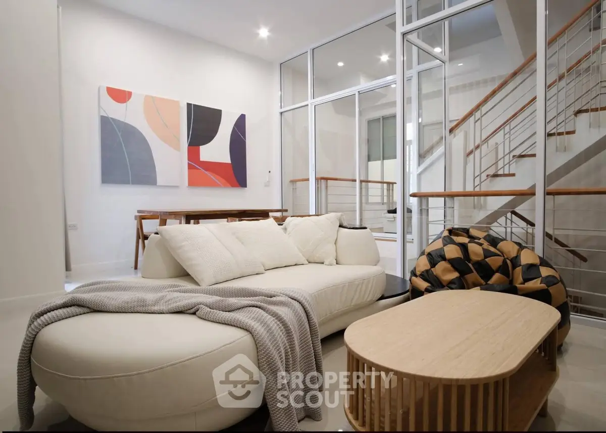 Modern living room with stylish furniture and abstract art, featuring a cozy sofa and elegant staircase.