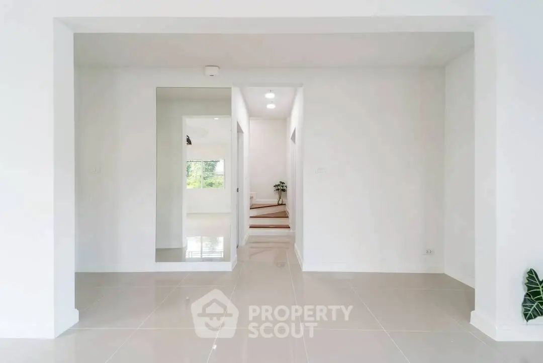 Bright minimalist hallway with glossy tiles and open doorway leading to stairs.