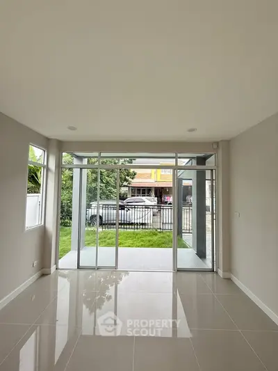 Spacious modern living room with large glass doors opening to a lush garden view.