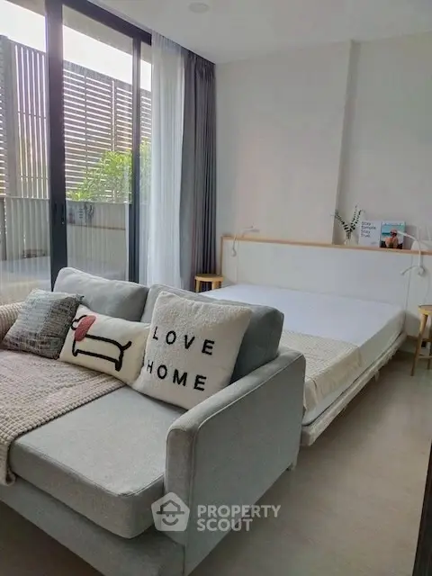 Cozy modern bedroom with stylish sofa and large windows opening to a private balcony.