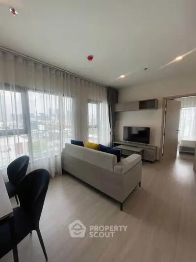 Modern living room with large windows and city view, featuring stylish furniture and open layout.