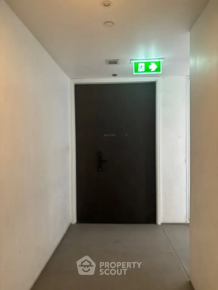 Modern building corridor with emergency exit sign above a dark door.