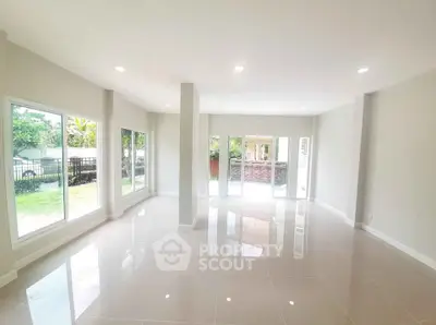 Spacious living room with large windows and glossy tile flooring, offering abundant natural light and garden view.
