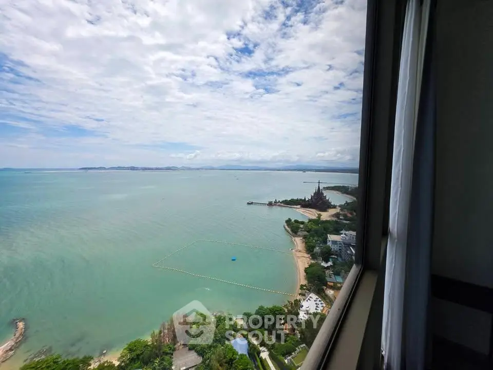 Stunning ocean view from high-rise building window, showcasing serene beach and lush greenery.