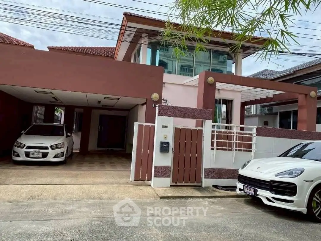 Modern two-story house with carport and luxury cars parked in driveway.
