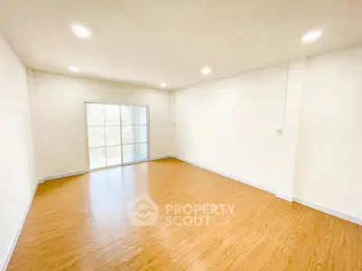 Spacious empty room with wooden flooring and large window, perfect for customization.