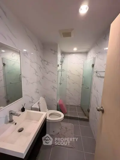 Modern bathroom with sleek fixtures and marble walls, featuring a glass-enclosed shower and stylish vanity.