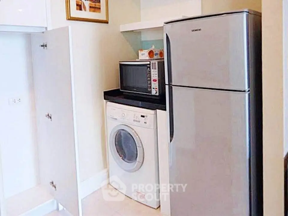 Modern kitchen with fridge, washing machine, and microwave in compact layout.