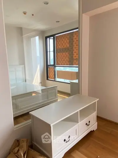 Bright bedroom with large window and stylish white furniture, featuring a mirrored wall for spacious feel.