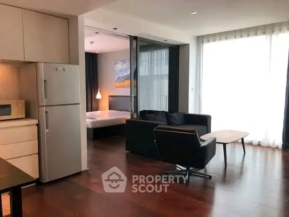 Modern open-plan living room with sleek kitchen and cozy bedroom area, featuring stylish furniture and natural light.