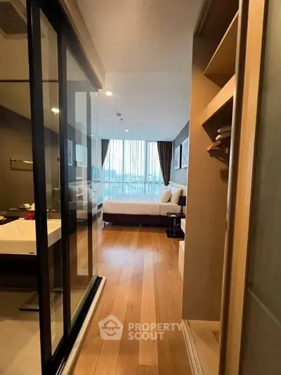 Modern bedroom with ensuite bathroom and wooden flooring, featuring a large window with city view.