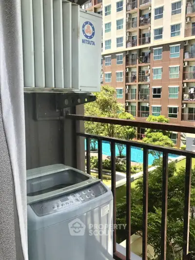 Condo balcony with washing machine overlooking pool and garden view.