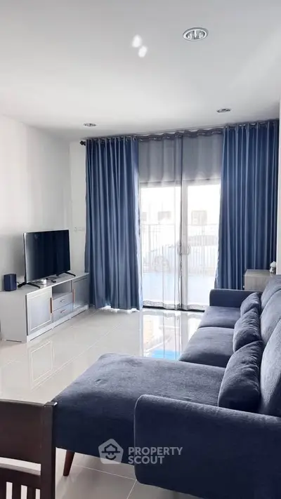 Modern living room with blue sofa and curtains, featuring a sleek TV setup.