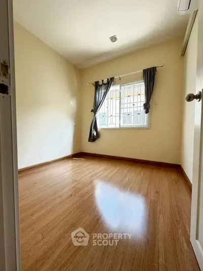 Spacious empty bedroom with wooden flooring and large window, perfect for customization.