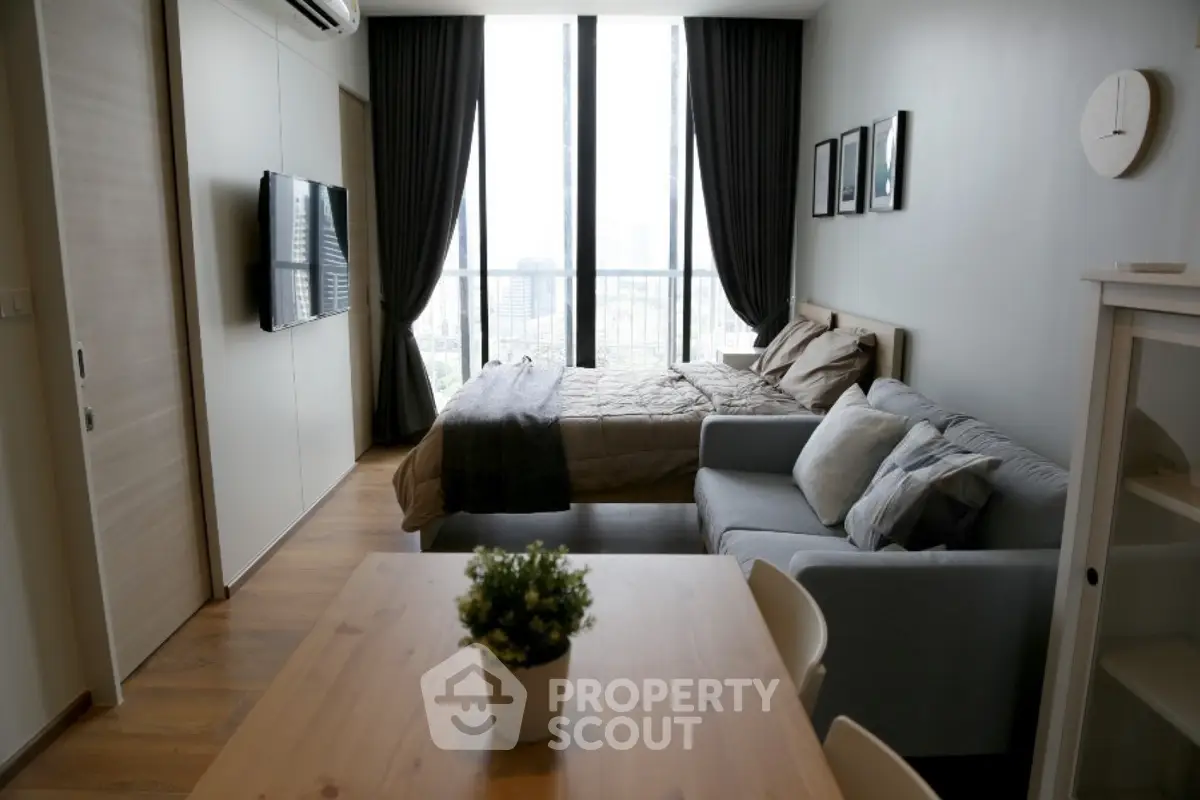 Modern studio apartment with cozy living area and large windows offering city views.