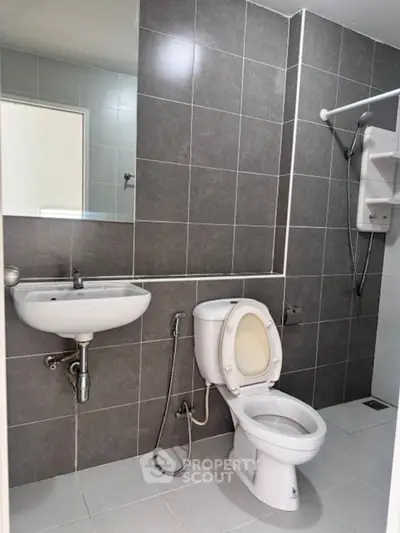 Modern bathroom with sleek gray tiles and white fixtures, featuring a toilet, sink, and shower area.
