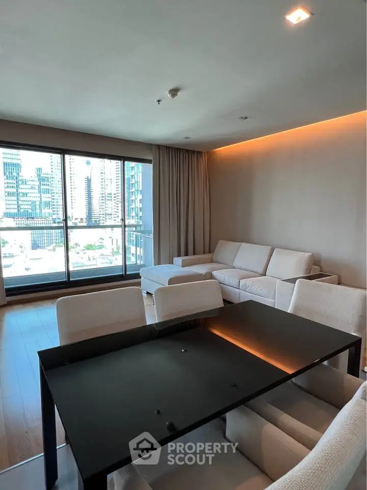 Spacious modern living room with city view, featuring elegant furniture and large windows.