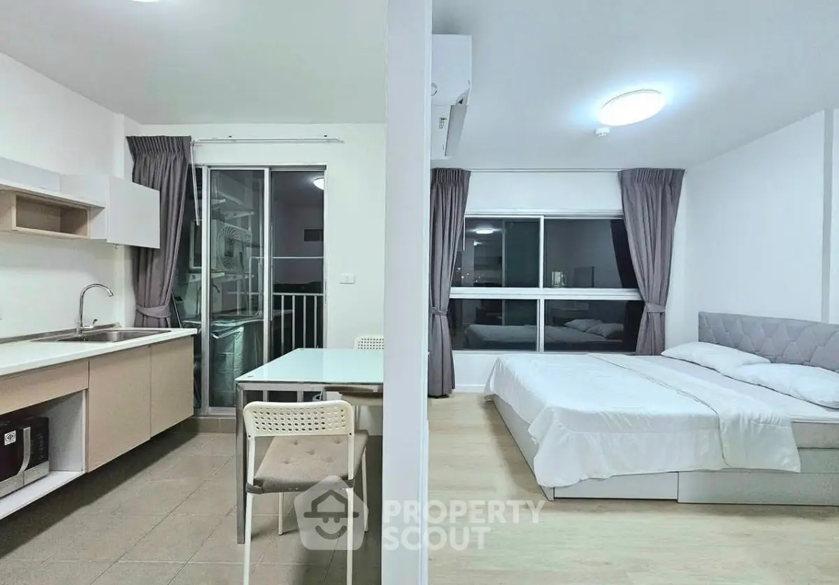 Modern studio apartment with open kitchen and cozy bedroom, featuring large windows and sleek furnishings.