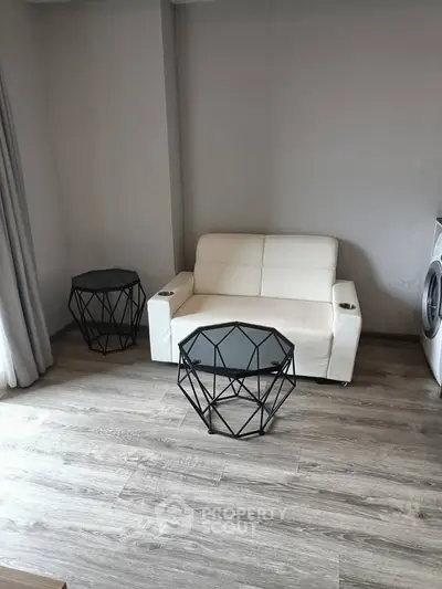 Modern living room with sleek white sofa and geometric tables on wooden flooring.