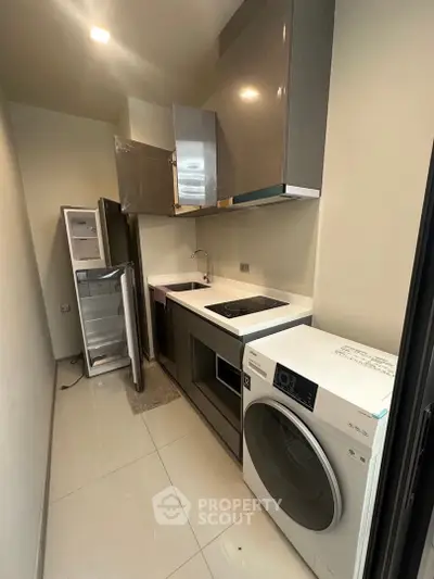 Modern compact kitchen with appliances including fridge and washing machine, sleek cabinetry, and induction cooktop.