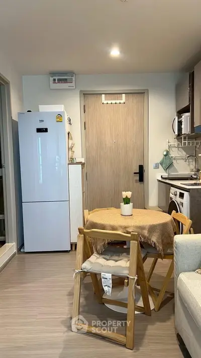 Cozy modern kitchen with dining area, featuring a fridge, washing machine, and stylish wooden furniture.