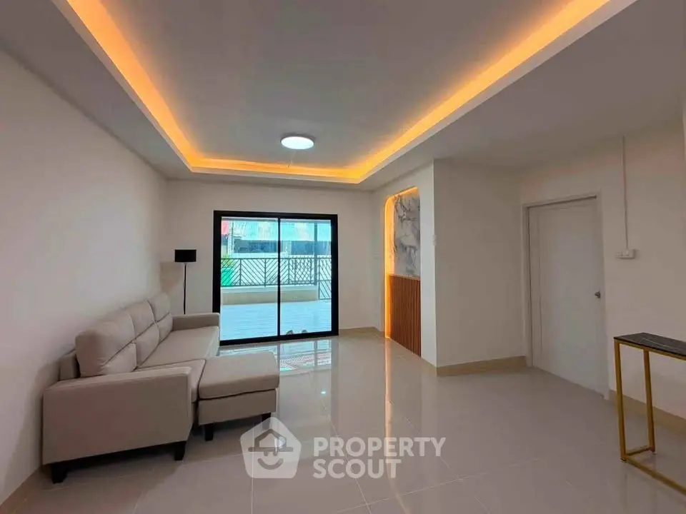 Modern living room with sleek design and large window leading to a balcony, featuring ambient ceiling lighting.