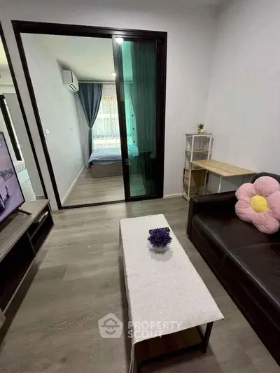 Modern living room with sleek furniture and view into cozy bedroom through glass doors.