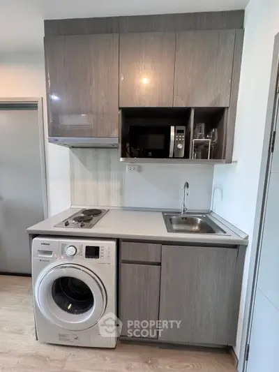 Compact modern kitchen with washing machine and microwave in sleek cabinetry.