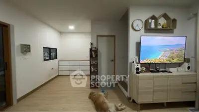Spacious living room with modern decor and wooden flooring, featuring a large TV and cozy ambiance.
