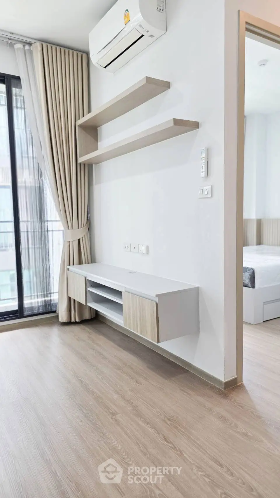 Modern living room with sleek shelving and air conditioning, featuring a view into a stylish bedroom.