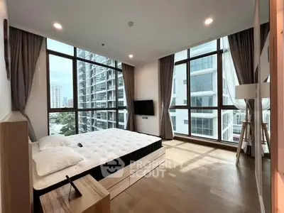 Spacious bedroom with floor-to-ceiling windows and modern decor in a high-rise apartment.