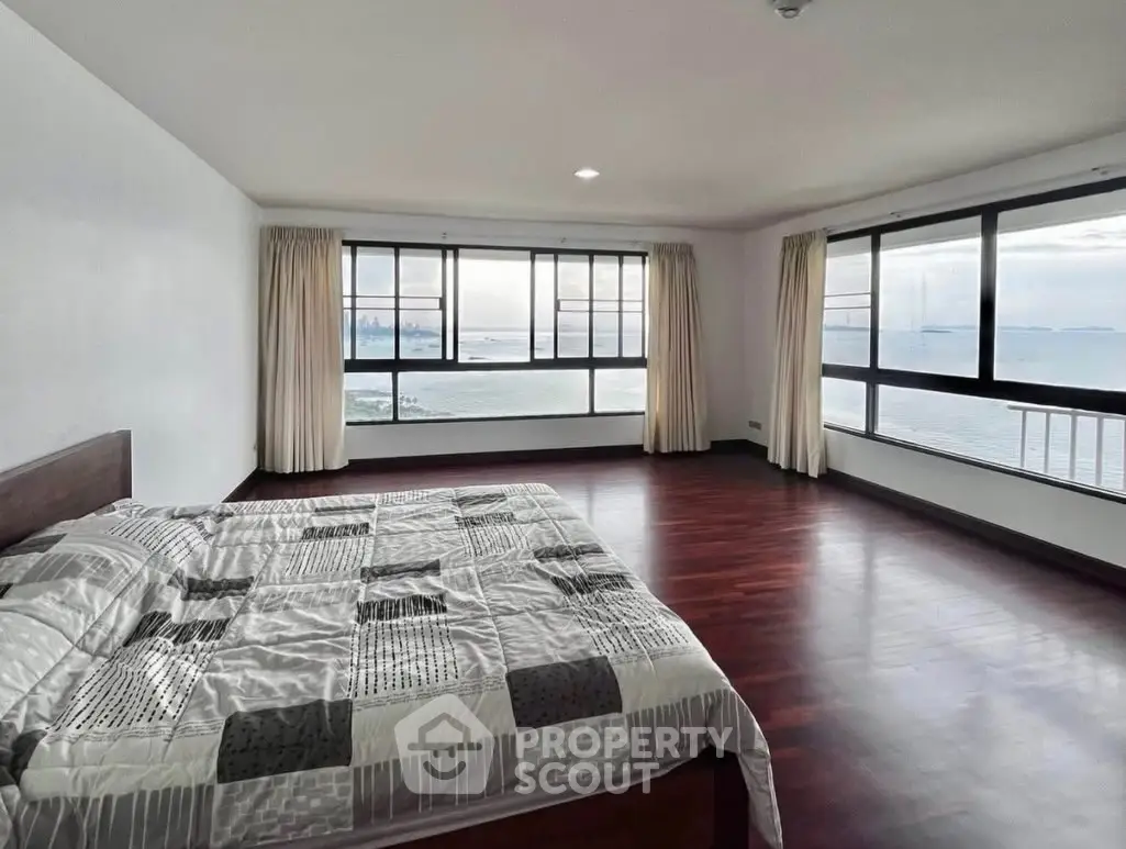 Spacious bedroom with stunning ocean view and large windows, featuring elegant wooden flooring.