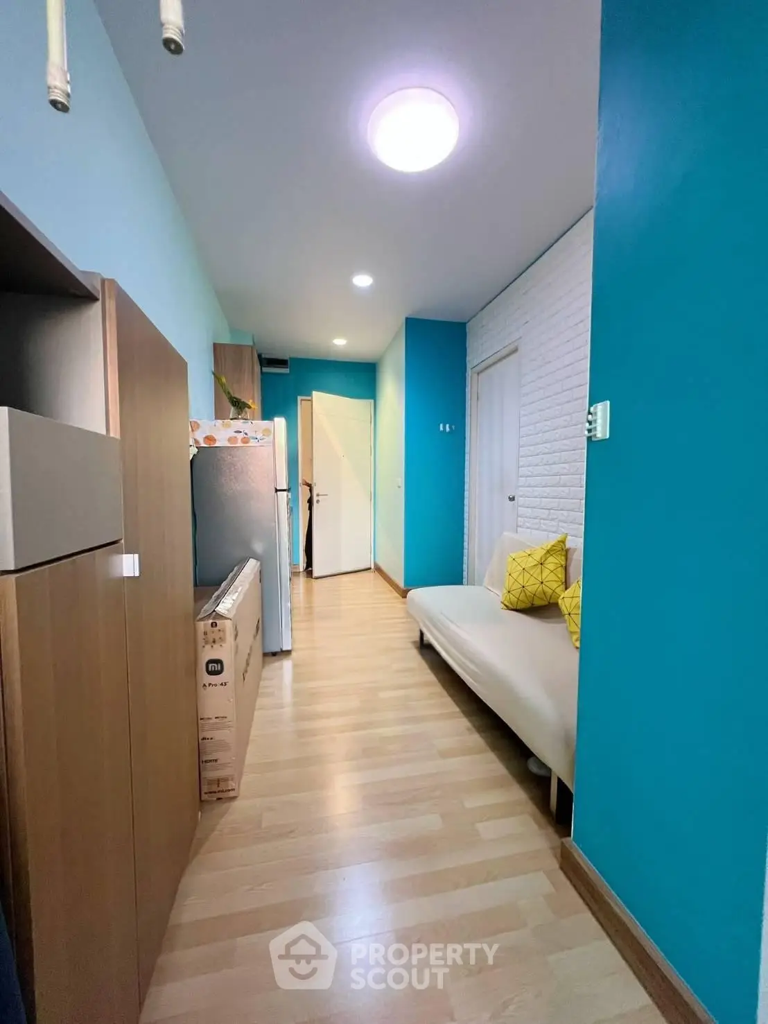 Charming apartment hallway with modern decor and bright blue walls, featuring a cozy sofa and sleek wooden flooring.