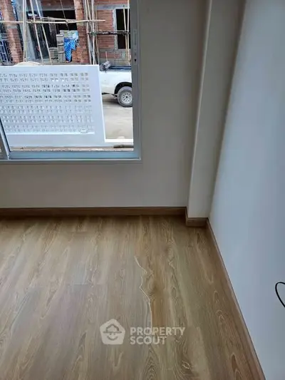 Modern interior with wooden flooring and large window, showcasing construction view outside.