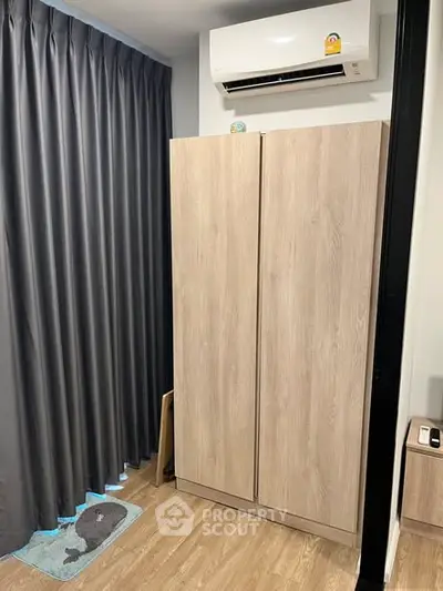 Modern bedroom with sleek wardrobe and air conditioning unit, featuring elegant wooden flooring and dark curtains.