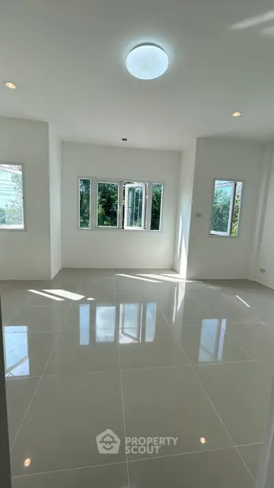 Spacious sunlit room with glossy tiled flooring and large windows offering lush green views.