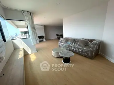 Spacious living room with large windows and modern furnishings in a high-rise apartment.