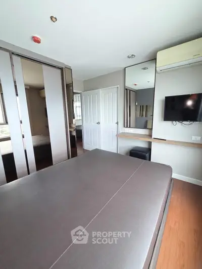 Modern bedroom with sleek design, featuring a wall-mounted TV, mirrored wardrobe, and air conditioning.
