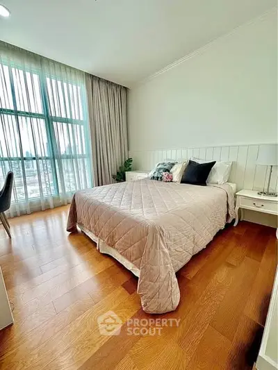 Spacious bedroom with elegant decor and large window offering natural light.