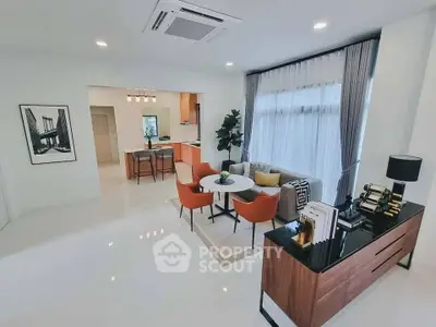 Modern living room with open kitchen, stylish furniture, and large window for natural light.