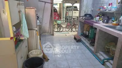 Rustic kitchen with open layout and tiled flooring, featuring basic appliances and storage shelves.