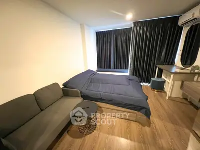 Modern bedroom with cozy bed, stylish sofa, and sleek wooden flooring.