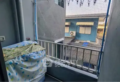 Compact balcony with protective netting and covered washing machine, overlooking neighboring buildings.