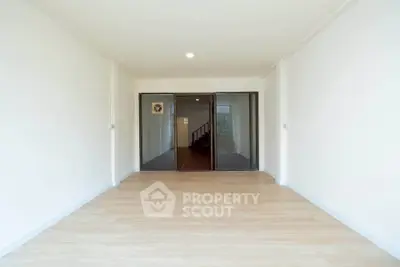 Spacious empty room with wooden flooring and glass doors leading to a hallway, ideal for customization.