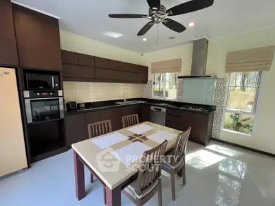 Modern kitchen with dark wood cabinets, dining table, and ceiling fan in a bright, airy space.