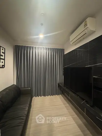Modern living room with sleek black sofa, large TV, and elegant curtains.