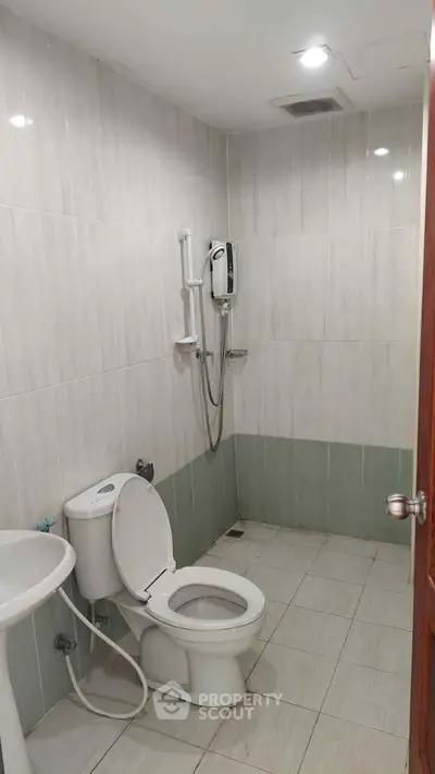 Modern bathroom with tiled walls and floor, featuring a toilet, sink, and shower area.