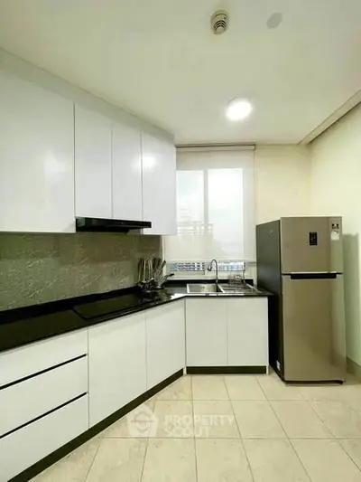 Modern kitchen with sleek white cabinets and stainless steel fridge in a bright apartment.