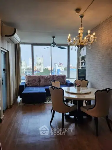 Elegant dining space with classic chandelier lighting, leading to a cozy living area with plush sofa and cityscape views through large windows.